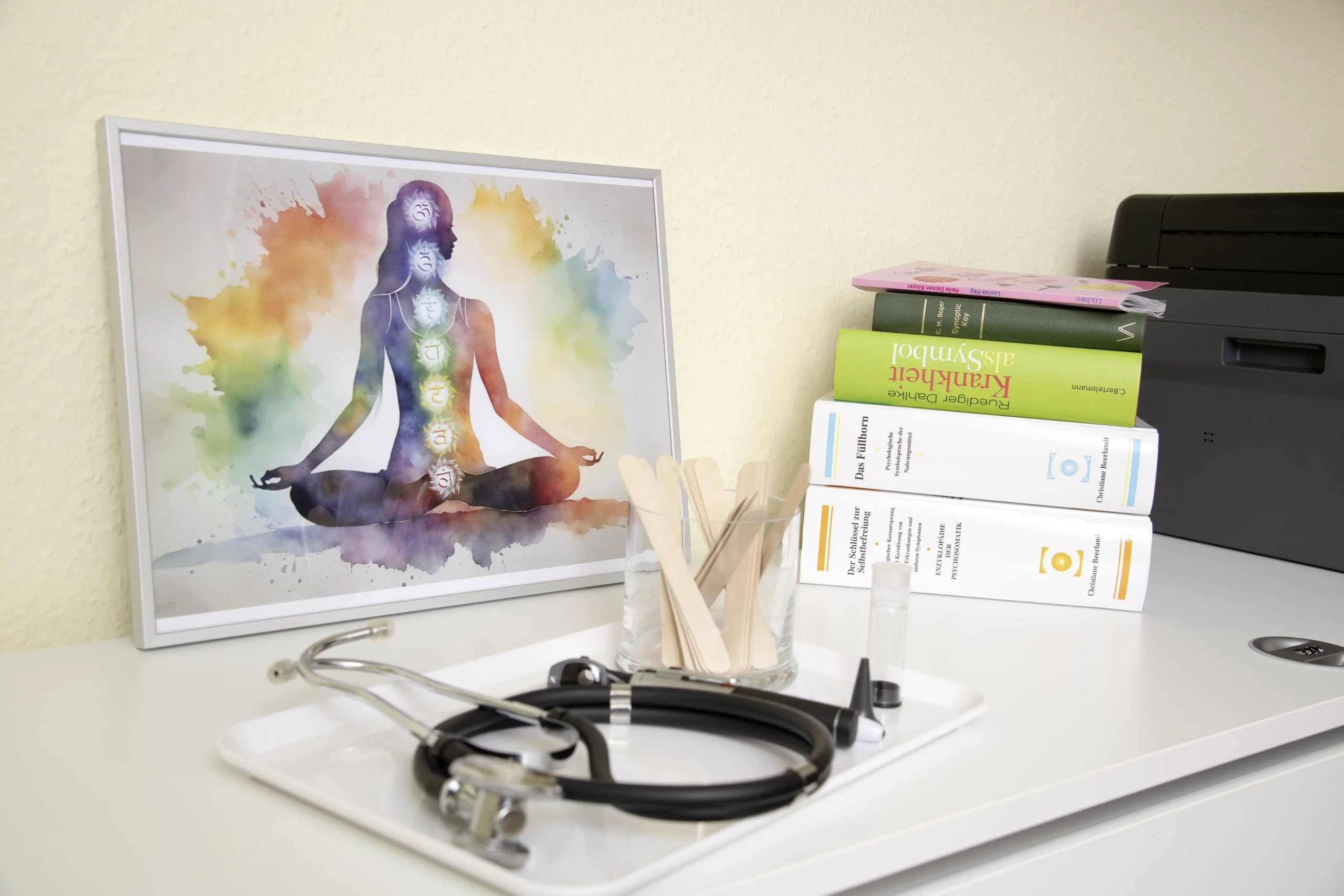 Auf einem Schrank liegen Fachliteratur, ein Bild zum Thema Energetik und ein Stethoskop.